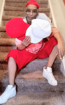 a man wearing red shorts is sitting on a set of stairs holding a red heart and a white hat