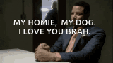 a man in a suit is sitting at a table and saying " my homie , my dog . i love you brah "