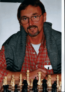 a man in a red plaid shirt is sitting at a chess board