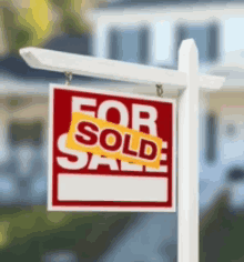 a red and white for sale sign is hanging from a white pole in front of a house .