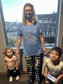 a woman wearing a blue shirt that says " where there is a wish let it be " stands next to two children