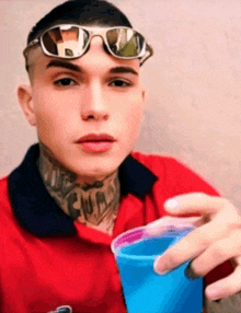 a young man wearing sunglasses holds a blue cup