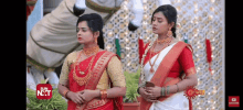 two women in red and white saris are standing next to each other in front of a horse statue .