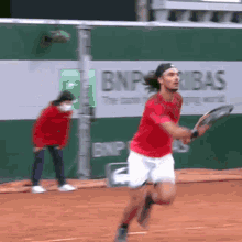 a man in a red shirt is running with a tennis racquet on a tennis court in front of a bnp advertisement