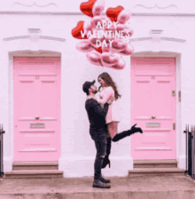 a man is holding a woman in his arms with balloons in the shape of hearts and the words happy valentine 's day