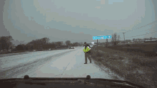 a man in a yellow vest stands on the side of a snowy road near a sign that says winterhage dr.