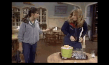 two women are standing next to each other in a restaurant with a bucket of ice and glasses on a table .