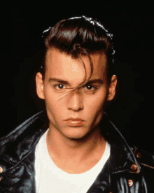 a young man wearing a black leather jacket and a white shirt looks at the camera