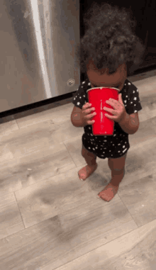 a baby is drinking from a red cup with the letter f on it