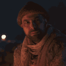 a man with a beard wearing a beanie and scarf looks down at something