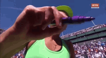 a woman in a green tank top is holding a purple marker in front of a crowd at a tennis match .