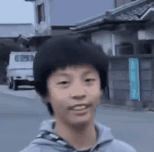 a young boy in a gray hoodie is standing on a street in front of a building .