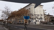 a stick figure stands in front of a building that says " ta trop la rage yaah "