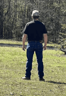 a man wearing a black shirt and blue jeans stands in a field