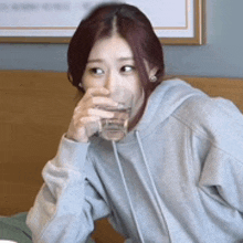 a woman in a gray hoodie is drinking a glass of water