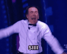 a man in a tuxedo and bow tie is screaming with the word siiii on his shirt