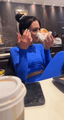 a woman in a blue outfit is eating a sandwich