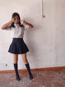 a girl in a white shirt and black skirt is pointing at herself