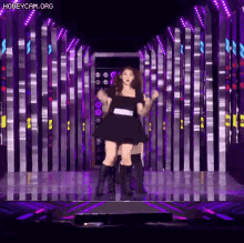 a woman in a black dress is dancing on a stage in front of a purple background .
