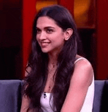 a woman with long hair is sitting on a couch smiling .