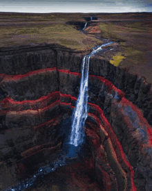 a waterfall is surrounded by a cliff with red stripes on it