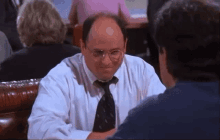 a man in a white shirt and tie is sitting at a table with another man .