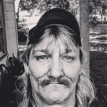 a black and white photo of a man with long hair and a beard wearing a hat .