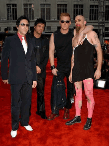 a group of men standing on a red carpet including one wearing pink tights