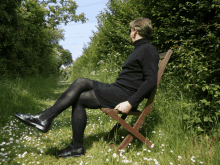 a man in a black dress is sitting in a chair in the grass