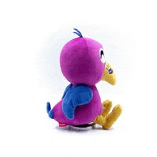 a purple stuffed animal with blue wings and a yellow beak is sitting on a table