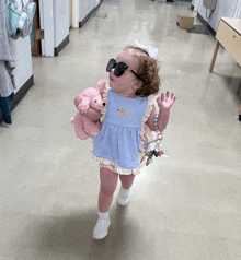 a little girl wearing sunglasses and a blue dress holds a pink teddy bear