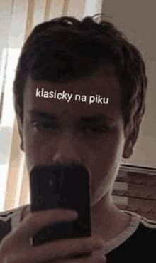 a young man is taking a selfie with a sticker on his forehead that says klasicky na piku .