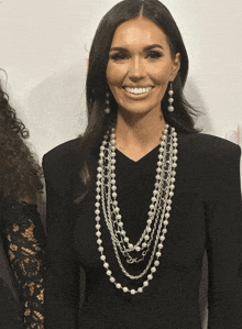 a woman wearing a black dress and a pearl necklace smiles for the camera