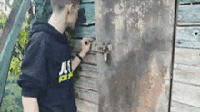 a man in a black hoodie is standing next to a wooden door .