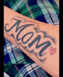 a woman has a tattoo of the word mom with a heart on her forearm .