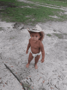 a baby wearing a diaper and a cowboy hat is standing in the dirt