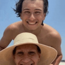 a man and a woman are posing for a picture on the beach . the woman is wearing a straw hat .