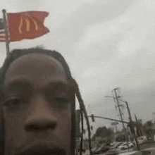 a man with dreadlocks is taking a selfie with a mcdonald 's flag flying over his head .