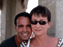 a man and a woman are posing for a picture in front of a wall with graffiti on it that says kou buck