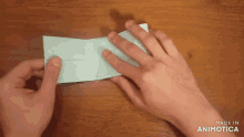 a person 's hands are folding a piece of paper on a table .