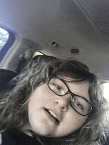 a girl wearing glasses is taking a selfie in a car