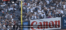 a crowd of people are watching a baseball game with a canon sign in the foreground