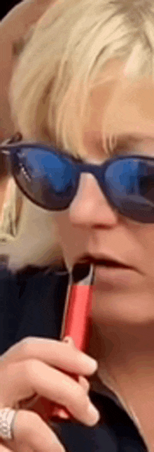 a woman wearing sunglasses is smoking a red e-cigarette .