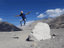 a man in a blue shirt is jumping in the air near a large rock