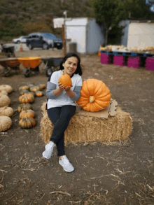 a woman sitting on a bale of hay holding a pumpkin