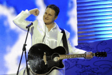 a man in a white suit holds a black guitar in front of a microphone