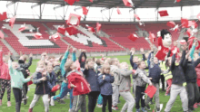 a group of children are throwing red hats in the air in front of a stadium with the letter b on it