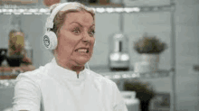 a woman wearing headphones is making a funny face while making a face in a kitchen .