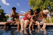 a group of people sit on the edge of a swimming pool