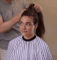 a woman is getting her hair done by a man wearing a striped cape